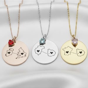 Könnte beinhalten: Drei Halsketten mit runden Anhängern, jeweils mit einer Kartenkontur mit Herzdetails und einem Edelstein. Eine ist roségoldfarben mit einem roten Herz, eine silberfarben mit einem blauen Edelstein und eine goldfarben mit einem rosa Edelstein.