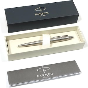 May include: A silver Parker pen with the name "Lilli" engraved on the side, presented in a cream-colored box with a white ribbon. The pen is displayed inside a black box with the Parker logo and text.