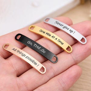 May include: Four metal shoe tags in rose gold, gold, black, and silver. Each tag has a different motivational phrase: "All things possible!", "Go, Trid, Go", "One Mile At A Time", and "Never give up!"
