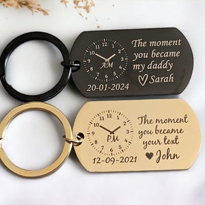May include: Two gold and black keychains with a clock face and the text "The moment you became my daddy" and "The moment you became your text" with the date and a heart symbol.