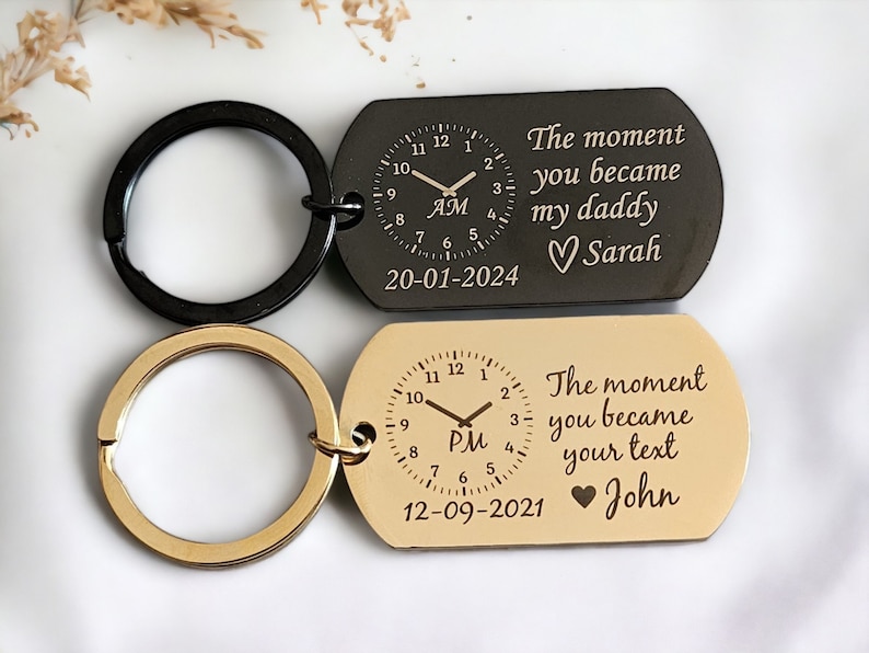 May include: Two gold and black keychains with a clock face and the text "The moment you became my daddy" and "The moment you became your text" with the date and a heart symbol.