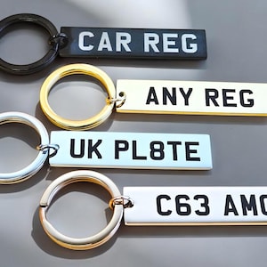 May include: Four different keychains with metal rings and rectangular tags. The tags are black, gold, silver, and white with black text. The text on the tags reads "CAR REG", "ANY REG", "UK PL8TE", and "C63 AMG".