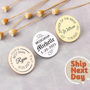 May include: Three round, gold, silver, and wood pins with black text. The gold pin says "Father of the Bride William 11.19.2023". The silver pin says "Bridegroom Michelle 5.20.2023". The wood pin says "Best Man Ryan 12.03.2023".