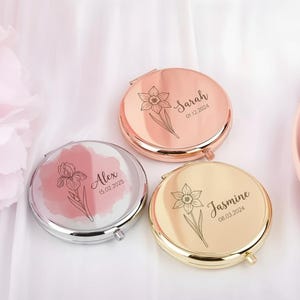 Könnte beinhalten: Drei personalisierte Kompaktspiegel in Roségold, Silber und Gold. Jeder Spiegel hat ein Blumendesign und einen Namen mit Datum. Die Namen sind Sarah, Alex und Jasmine. Die Spiegel sind rund und haben eine Klappöffnung.