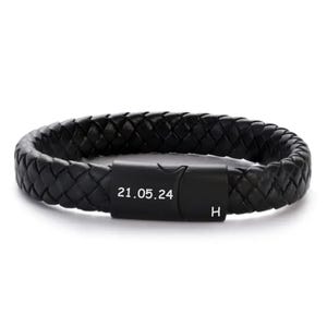 May include: Black braided leather bracelet with a matte black clasp. The clasp features the date "21.05.24" and the letter "H". The bracelet is a stylish accessory.