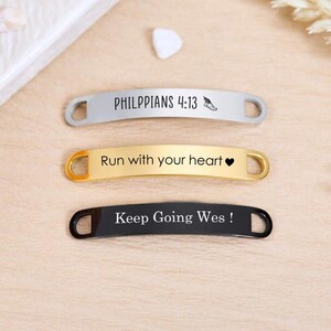 May include: Three metal shoe tags in silver, gold, and black. The silver tag reads "PHILIPPIANS 4:13" with a small shoe graphic. The gold tag says "Run with your heart" and has a heart symbol. The black tag says "Keep Going Wes!"