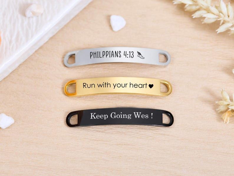 May include: Three metal shoe tags in silver, gold, and black. The silver tag reads "PHILIPPIANS 4:13" with a small shoe graphic. The gold tag says "Run with your heart" and has a heart symbol. The black tag says "Keep Going Wes!"