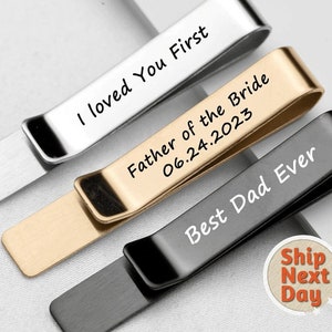 May include: Three tie clips with different engravings. The first tie clip is silver and says "I loved you first". The second tie clip is gold and says "Father of the Bride 06.24.2023". The third tie clip is black and says "Best Dad Ever".