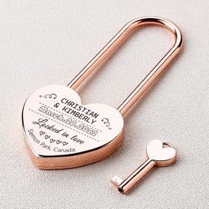 May include: Rose gold heart-shaped padlock with a key. The padlock has an inscription that reads "Christian & Kimberly March 28, 2022 Locked in love Slemon Park, Canada".