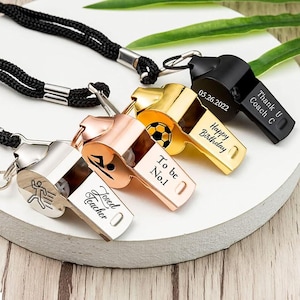 Pode incluir: Uma coleção de apitos de metal personalizados em prata, ouro rosa, dourado e preto. Cada apito tem um cordão preto e apresenta texto gravado como "Loved Teacher", "To be No.1", "Happy Birthday" e "Thank U Coach C".
