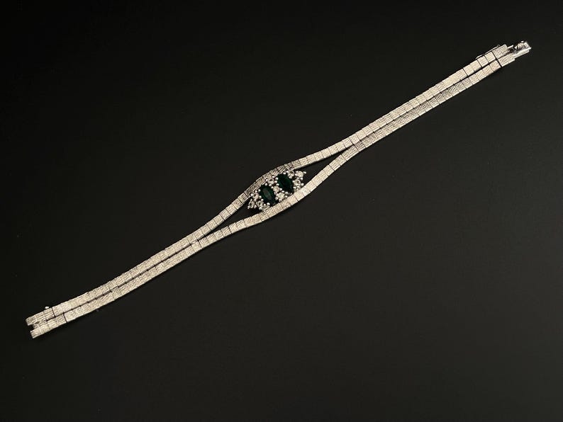 May include: A silver bracelet with a double row of clear stones and a centrepiece of three green stones.