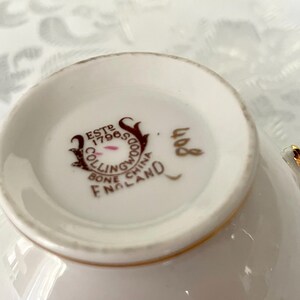 Puede incluir: Primer plano del interior de una taza de t&eacute; blanca con borde dorado. La base de la taza presenta un logotipo marr&oacute;n y dorado que dice "ESTD 17965 COLLINGWOOD BONE CHINA ENGLAND". El n&uacute;mero "408" est&aacute; impreso en dorado.