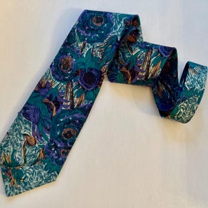 Pode incluir: Uma gravata com um padr&atilde;o vibrante de formas florais em azul-petr&oacute;leo, roxo e azul-escuro. O design inclui linhas onduladas e elementos bot&acirc;nicos abstratos sobre um fundo azul-petr&oacute;leo claro, criando uma textura visual densa e em camadas.