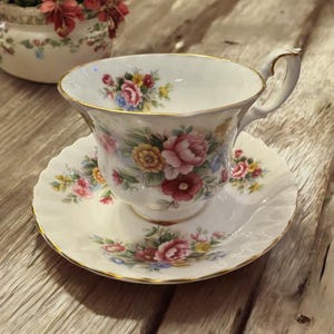 May include: A white teacup and saucer with a floral pattern. The cup has a gold rim and the saucer has a scalloped edge.