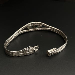 May include: A silver chain bracelet with a decorative clasp. The bracelet is made of multiple strands of linked metal.