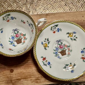 Pu&ograve; includere: Un set da t&egrave; vintage composto da una tazza e un piattino con un motivo floreale. La tazza e il piattino sono bianchi con un bordo dorato e presentano un delicato disegno floreale con fiori rosa, gialli e blu. Il disegno include un cestino di fiori con un fiocco.