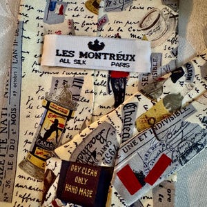 Pu&ograve; includere: Una cravatta in seta color crema con una stampa d'ispirazione vintage di francobolli francesi, scrittura a mano e monumenti parigini. Un'etichetta bianca riporta LES MONTREUX ALL SILK PARIS e una scura indica DRY CLEAN ONLY HAND MADE.