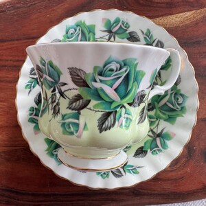 May include: A vintage teacup and saucer set with a green and white floral pattern. The cup and saucer have a gold trim and a delicate scalloped edge.