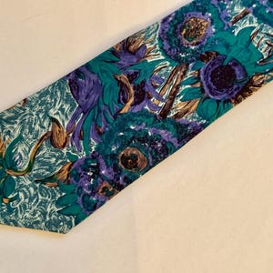 Pode incluir: Uma gravata com um padr&atilde;o floral vibrante em tons de azul-petr&oacute;leo, roxo e castanho. O design apresenta grandes motivos florais pict&oacute;ricos sobre um fundo azul-petr&oacute;leo texturizado, criando um aspeto visual arrojado e colorido.