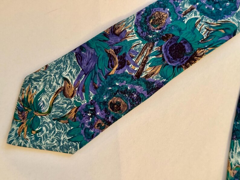 Pode incluir: Uma gravata com um padr&atilde;o floral vibrante em tons de azul-petr&oacute;leo, roxo e castanho. O design apresenta grandes motivos florais pict&oacute;ricos sobre um fundo azul-petr&oacute;leo texturizado, criando um aspeto visual arrojado e colorido.