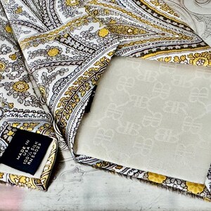 May include: A silk tie with a paisley pattern in white, gold, and gray. The tie has a label that reads "Made in USA 100% Silk". The back of the tie is a cream color with a repeating pattern.
