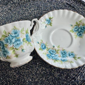 May include: A white teacup and saucer set with a blue floral pattern. The cup and saucer have a scalloped edge.