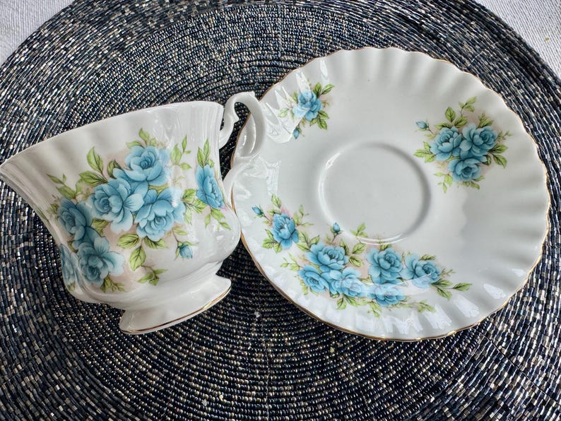 May include: A white teacup and saucer set with a blue floral pattern. The cup and saucer have a scalloped edge.