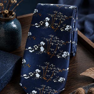 May include: A dark blue necktie featuring a repeating pattern of black and white pandas eating bamboo stalks. The design includes small brown and white details depicting the pandas in various positions among the bamboo plants.