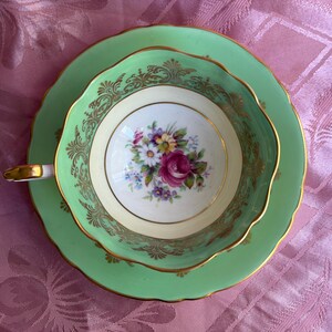Peut inclure: Une tasse &agrave; th&eacute; et sa soucoupe vert clair avec un bord festonn&eacute; et une bordure dor&eacute;e. L'int&eacute;rieur de la tasse pr&eacute;sente un bouquet floral central avec des fleurs roses, jaunes et violettes sur fond blanc, rehauss&eacute; par un filigrane dor&eacute; orn&eacute;.