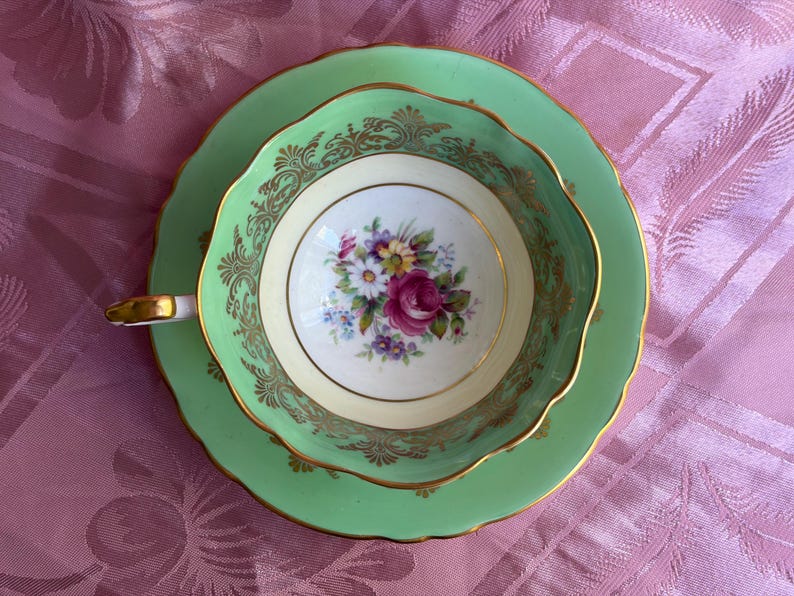 Peut inclure: Une tasse &agrave; th&eacute; et sa soucoupe vert clair avec un bord festonn&eacute; et une bordure dor&eacute;e. L'int&eacute;rieur de la tasse pr&eacute;sente un bouquet floral central avec des fleurs roses, jaunes et violettes sur fond blanc, rehauss&eacute; par un filigrane dor&eacute; orn&eacute;.