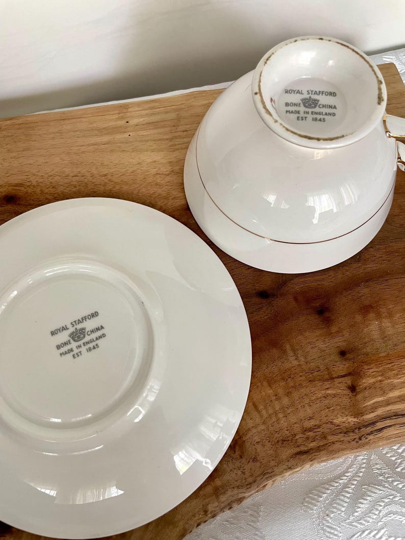Pode incluir: Um conjunto de ch&aacute;vena e pires de porcelana Royal Stafford branca. A ch&aacute;vena e o pires s&atilde;o brancos com detalhes dourados. O log&oacute;tipo e o texto Royal Stafford est&atilde;o no pires e na base da ch&aacute;vena. Fabricado na Inglaterra em 1845.