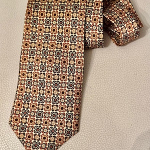 May include: A necktie featuring a repeating geometric pattern of small, stylized four-petaled floral shapes in shades of dark brown, rust orange, and cream. The fabric has a smooth, slightly reflective finish, and the tie is folded at the top.
