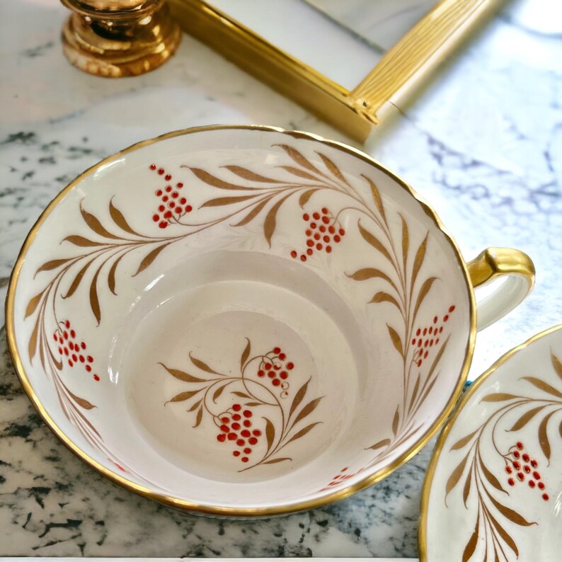Pu&ograve; includere: Servizio da t&egrave; color crema con finiture dorate e un motivo decorativo di foglie marroni e bacche rosse. La tazza ha un manico dorato. Il set &egrave; probabilmente vintage o antico.