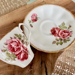 Pu&ograve; includere: Un set da t&egrave; bianco con bordo dorato e design floreale con rose rosa. La tazza da t&egrave; ha un manico e il piattino ha un bordo ondulato.