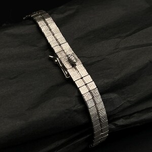 May include: A silver bracelet with a square link design. The bracelet has a clasp closure.
