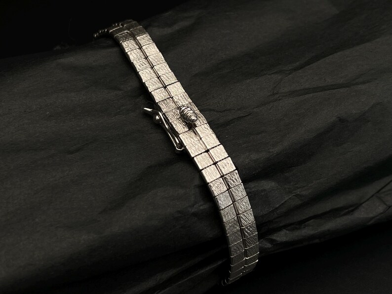 May include: A silver bracelet with a square link design. The bracelet has a clasp closure.