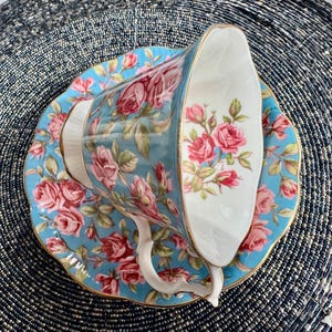 K&ouml;nnte beinhalten: Ein blaues und wei&szlig;es Tee-Set mit einem Blumenmuster aus rosa Rosen. Tasse und Untertasse haben einen goldenen Rand.