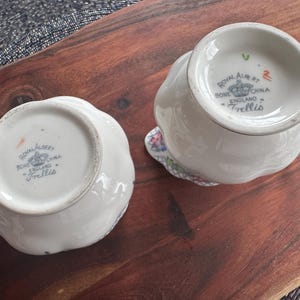 Pu&ograve; includere: Due brocche per panna e zucchero in porcellana bianca con motivi floreali e le parole "Royal Albert Bone China England Trellis" sul fondo.