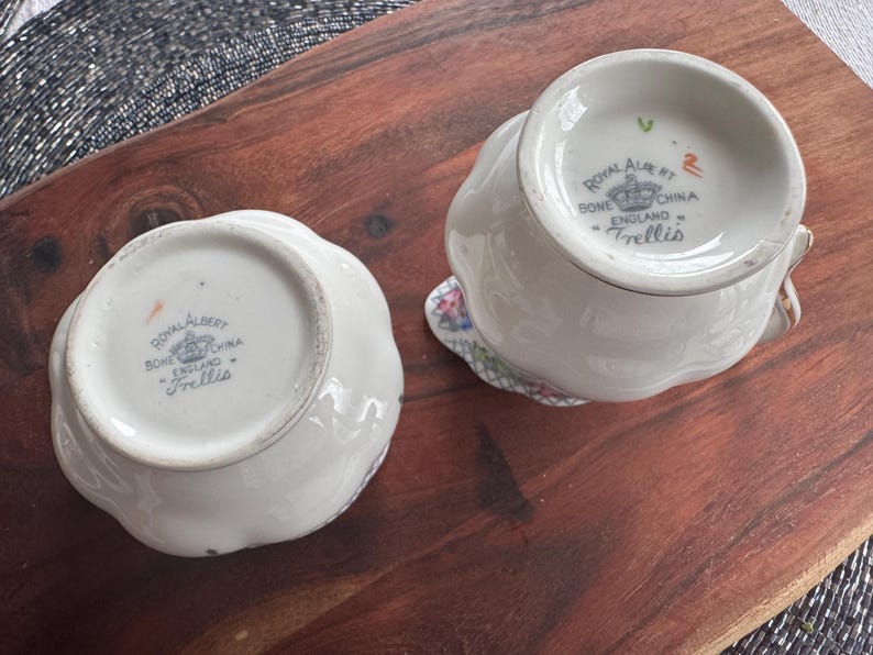 Pu&ograve; includere: Due brocche per panna e zucchero in porcellana bianca con motivi floreali e le parole "Royal Albert Bone China England Trellis" sul fondo.