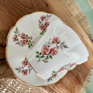 May include: A white teacup and saucer with a gold rim and floral pattern. The flowers are pink and green and are arranged in a delicate pattern.