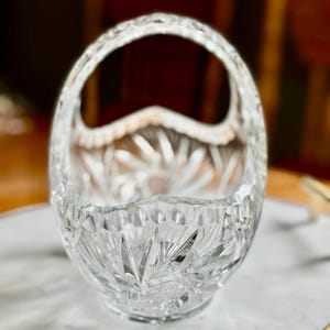 May include: A clear, cut-glass basket with a handle. The basket has a starburst pattern on the base and sides, with a scalloped rim. The handle is also cut glass. This decorative basket is ideal for displaying small items or as a centerpiece.