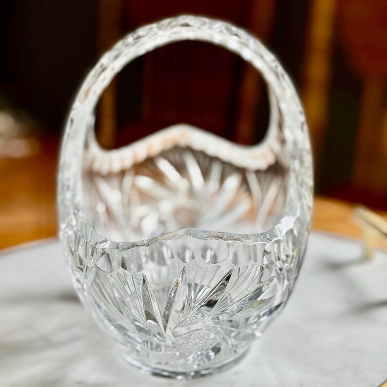 May include: A clear, cut-glass basket with a handle. The basket has a starburst pattern on the base and sides, with a scalloped rim. The handle is also cut glass. This decorative basket is ideal for displaying small items or as a centerpiece.