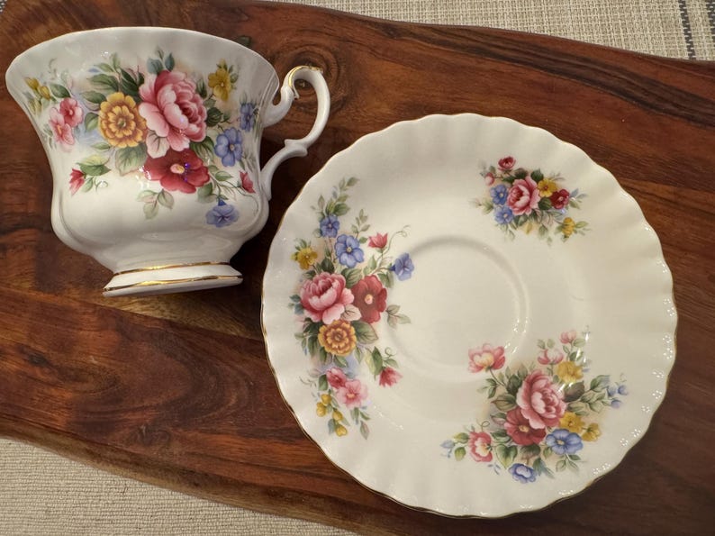 May include: A white teacup and saucer with a floral pattern. The cup and saucer have a gold trim. The flowers are pink, red, yellow, and blue.