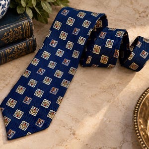 May include: A deep blue necktie featuring a repeating pattern of small, square-framed motifs. Each square contains a central red and gold emblem surrounded by light blue and white borders, set against a textured, dark blue fabric background.