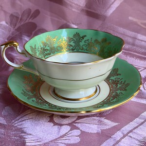 Peut inclure: Un ensemble tasse &agrave; th&eacute; et soucoupe en porcelaine avec un motif vert menthe et blanc. Le bord de la tasse et le pourtour de la soucoupe sont orn&eacute;s de motifs en filigrane dor&eacute;s complexes. La tasse poss&egrave;de une base sur pied et une anse dor&eacute;e.