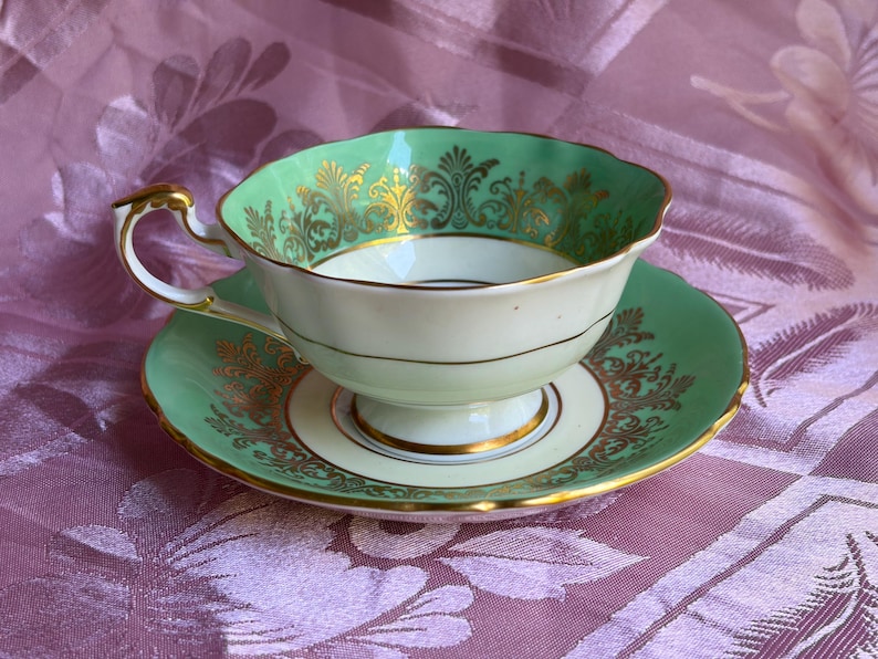 Peut inclure: Un ensemble tasse &agrave; th&eacute; et soucoupe en porcelaine avec un motif vert menthe et blanc. Le bord de la tasse et le pourtour de la soucoupe sont orn&eacute;s de motifs en filigrane dor&eacute;s complexes. La tasse poss&egrave;de une base sur pied et une anse dor&eacute;e.