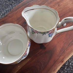 Pu&ograve; includere: Un set di brocca per la panna e zuccheriera in porcellana bianca con un motivo floreale in tonalit&agrave; rosa, blu e giallo. Il set ha un bordo dorato.