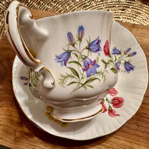 May include: A white teacup and saucer with a floral pattern. The cup has a gold rim and a delicate handle. The saucer has a scalloped edge.