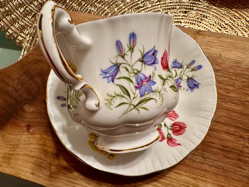 May include: A white teacup and saucer with a floral pattern. The cup has a gold rim and a delicate handle. The saucer has a scalloped edge.