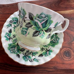 May include: A white teacup and saucer with a green and white floral pattern. The cup and saucer have a gold trim.